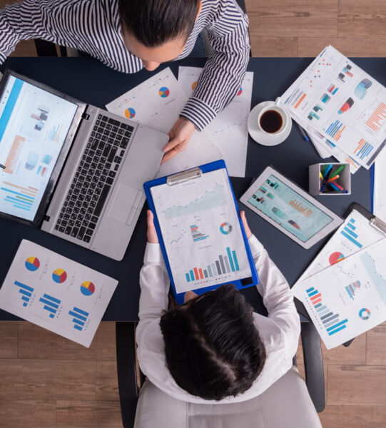 Top view of manager and employee doing teamwork Top viewTop view of manager and employee doing teamwork in business office , looking at charts on laptop display. Finance paperwork with charts at workplace. Discusing financial plan.